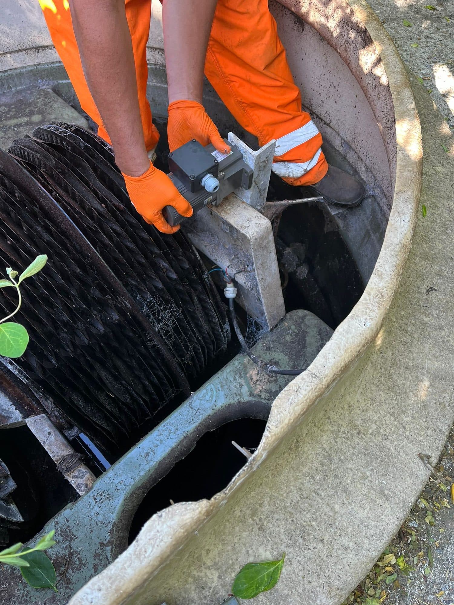 Engineer in orange protective overalls and gloves servicing the rotating biodisc inside a sewage treatment plant